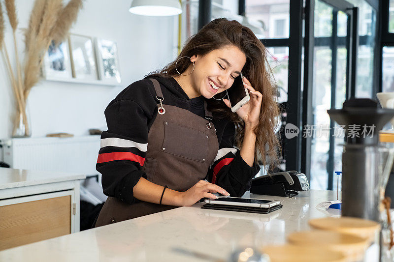 穿着制服的年轻女咖啡师在咖啡店打电话