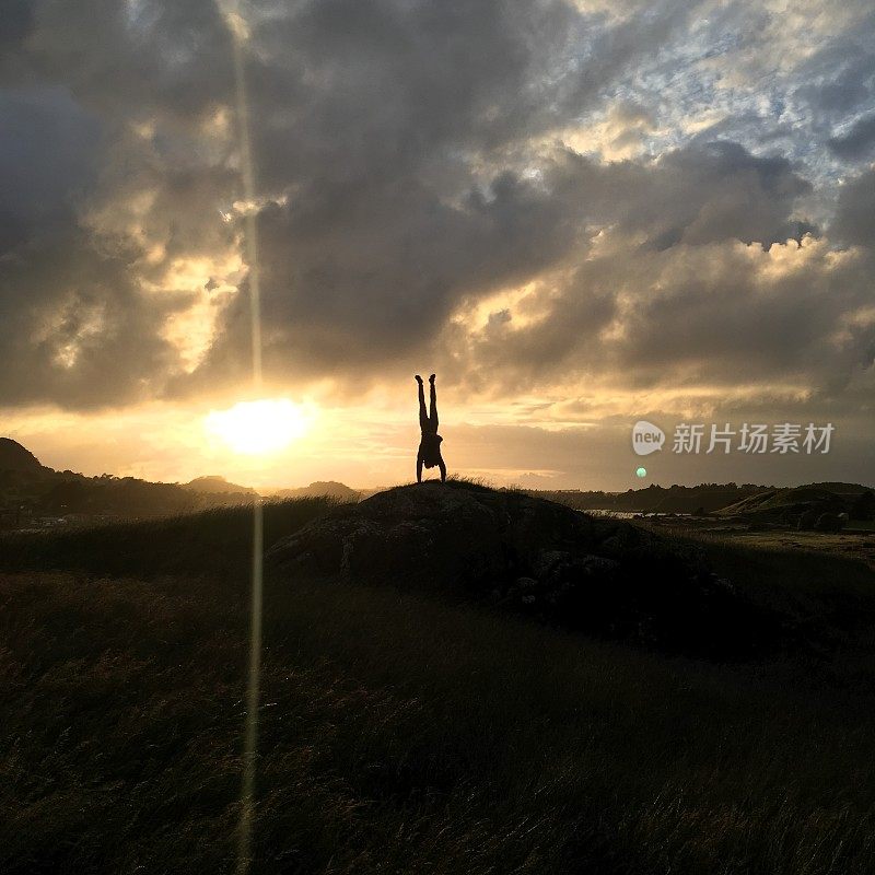 夕阳下，一个男人在山顶上倒立的剪影