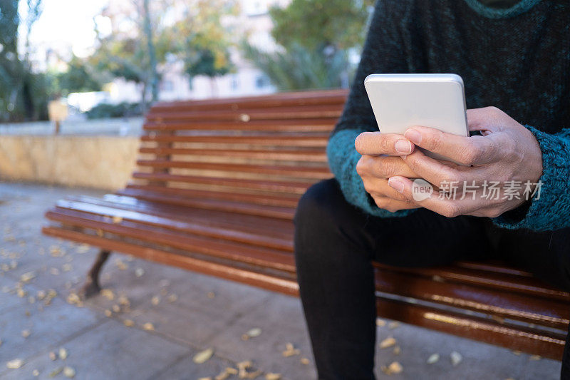 一位忧心忡忡的孤独女子坐在公园的长椅上用她的智能手机