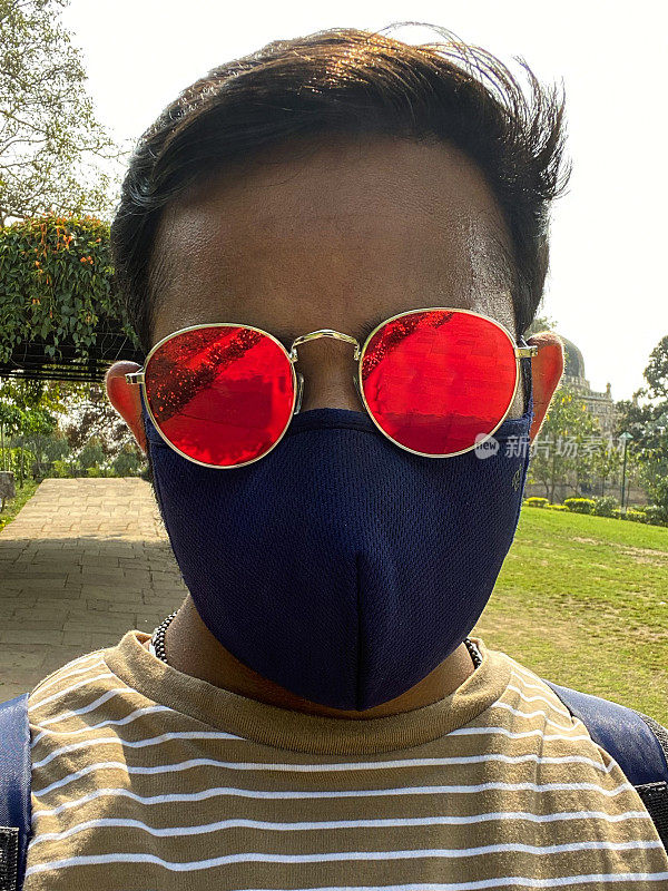 在全球突发卫生事件、隔离和疾病期间，一名印度男子在户外戴着太阳镜和医用口罩保护冠状病毒Covid-19病毒，戴着口罩