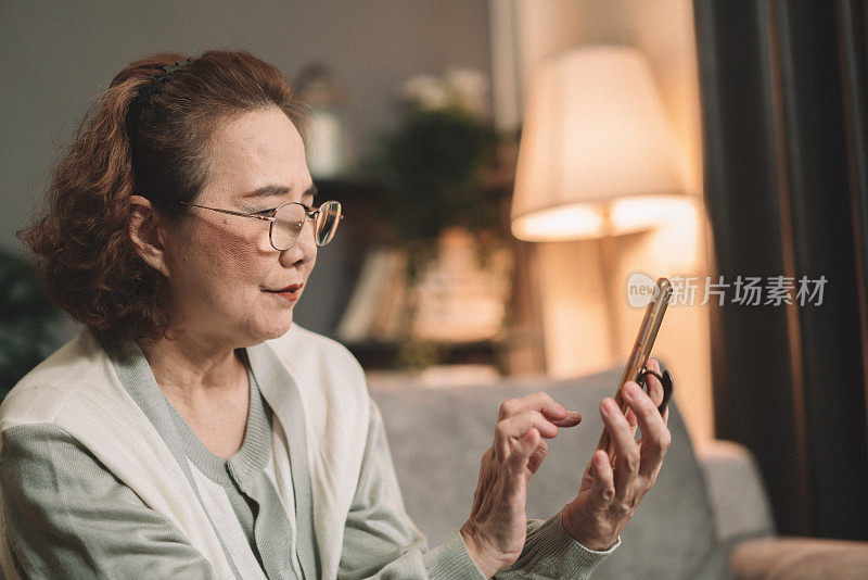在家里发短信或用智能手机聊天时微笑。年长的女性或祖母在客厅里拿着手机玩社交媒体或在线播客。精通技术概念