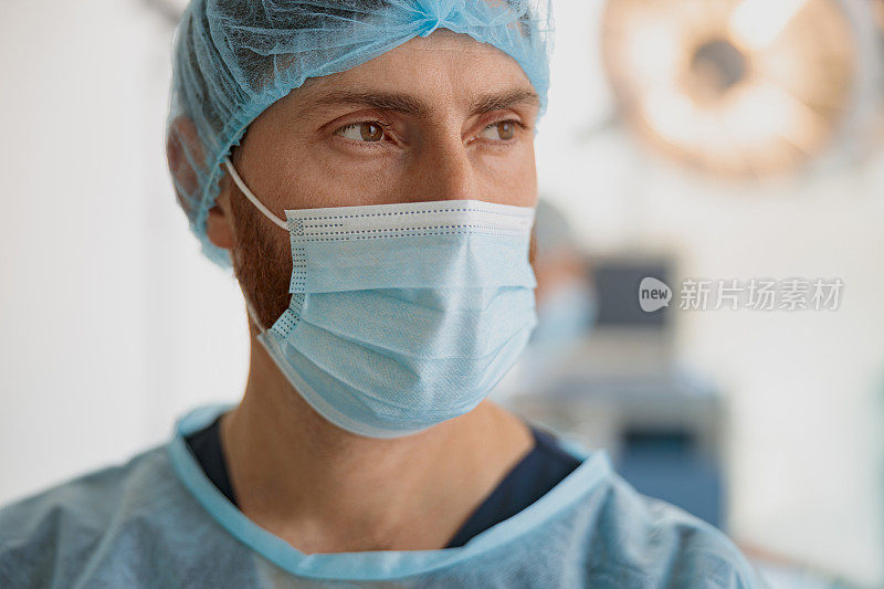 戴口罩的专业医生在手术前站在手术室，看向别处的特写