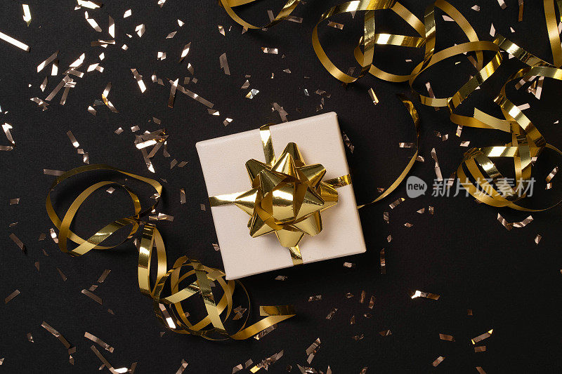 黑色背景上的金色蝴蝶结和金色纸屑的白色小礼盒