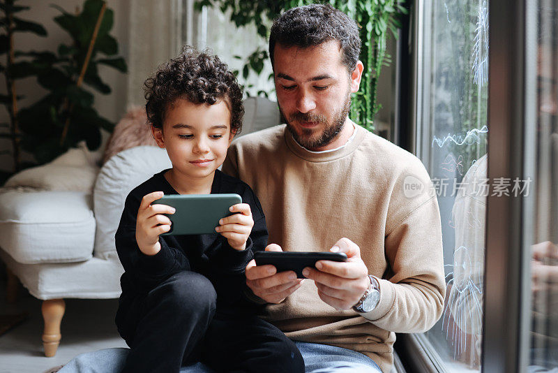 快乐的年轻父亲和儿子一起在智能手机上玩电子游戏