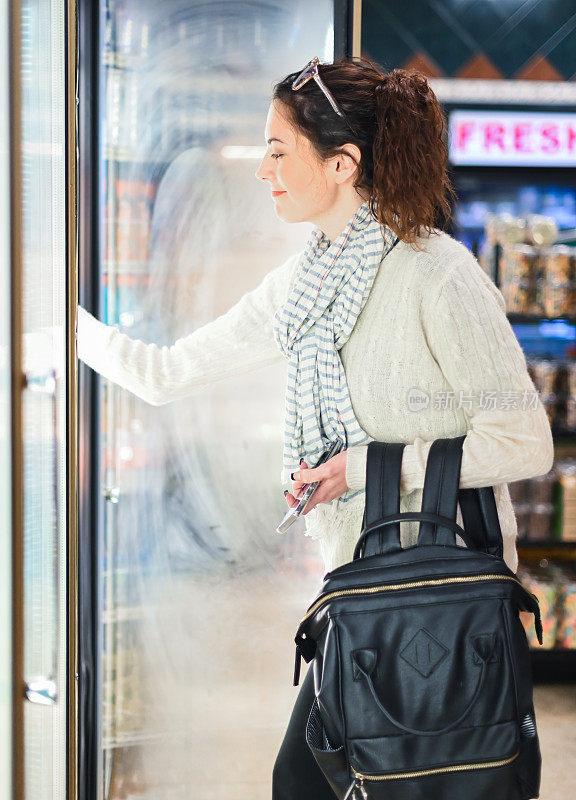 一位女士在杂货店、便利店或机场的冷藏区挑选食物