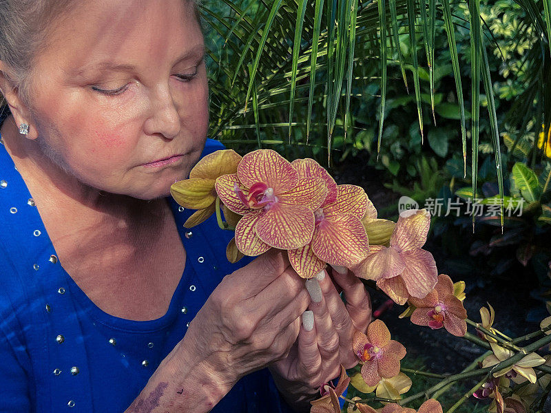 中年妇女在宁静的花园里闻着兰花的味道