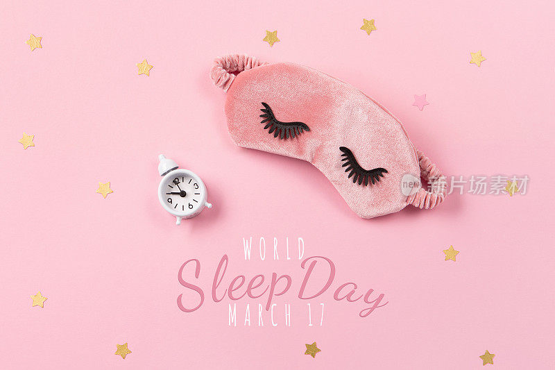 世界睡眠日定在3月。可爱的睡眠面具和闹钟在粉红色粉彩背景，俯视图。