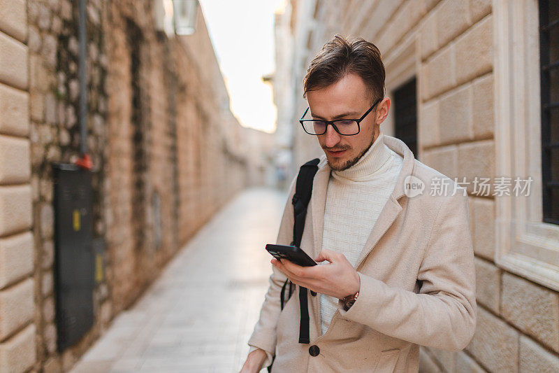 英俊的年轻人在度假时使用他的手机参观一个老城区