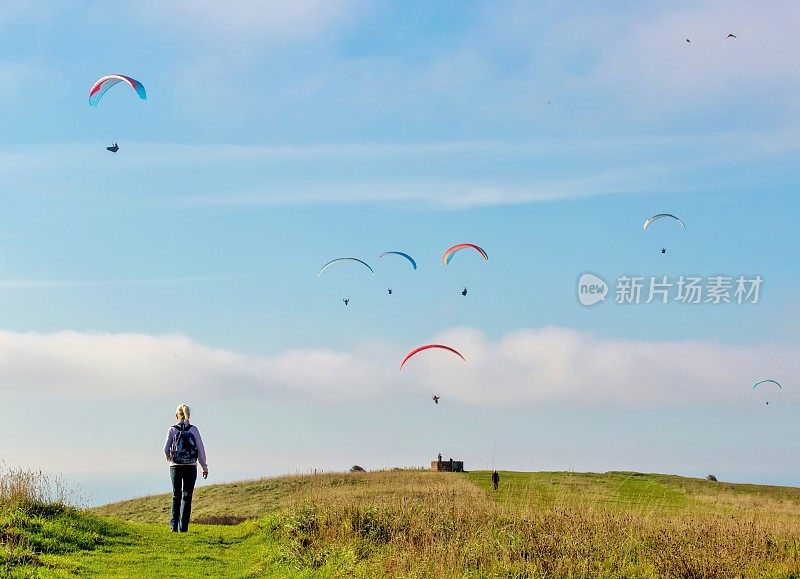 英国东苏塞克斯郡，一名徒步旅行者接近在比奇角上空飞行的滑翔伞