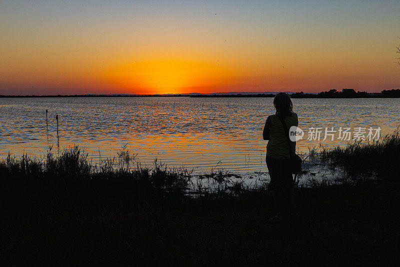 后视图的妇女看美丽的日落在湖岸