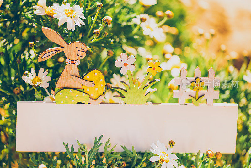 在一个鲜花盛开的花园里，一个空的复活节板上有一个可爱的兔子和鸡蛋装饰，作为你的复活节短信的模型