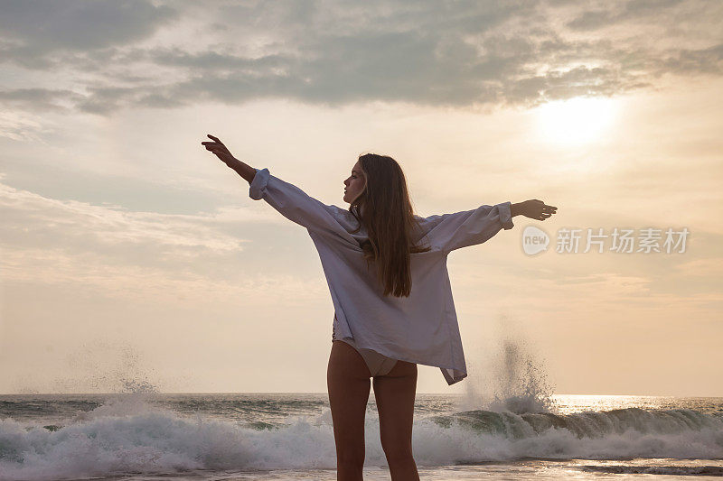 后视图苗条的年轻女子在白色衬衫摆姿势与手侧在海洋背景。在热带海上享受轻松愉快的假期。旅游度假概念，暑假。复制广告文字空间