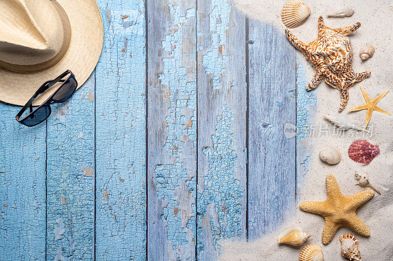 夏天，海滩和度假的概念与自由文本空间。前视图。平面布局有一个男人草帽，太阳眼镜，大海星和海贝壳和各种海贝壳和细沙滩在一个古老的蓝色木板背景