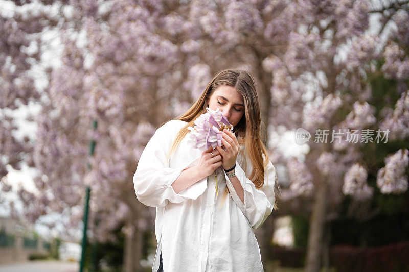 春天里，年轻女子手持鲜花站在盛开的树前。春天的概念