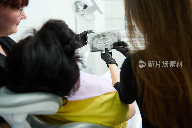牙科实践。牙科医生的后视图解释病人在牙科诊所预约时的牙齿x光片
