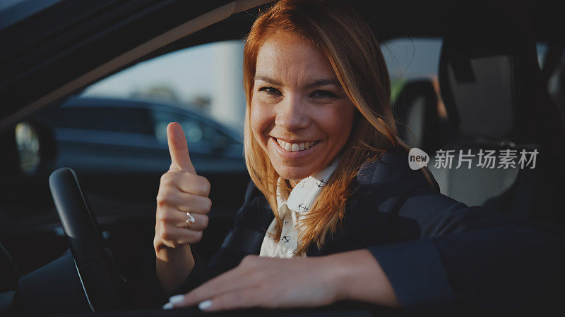 一位兴高采烈的女商人坐在新车里，在经销商面前竖起大拇指