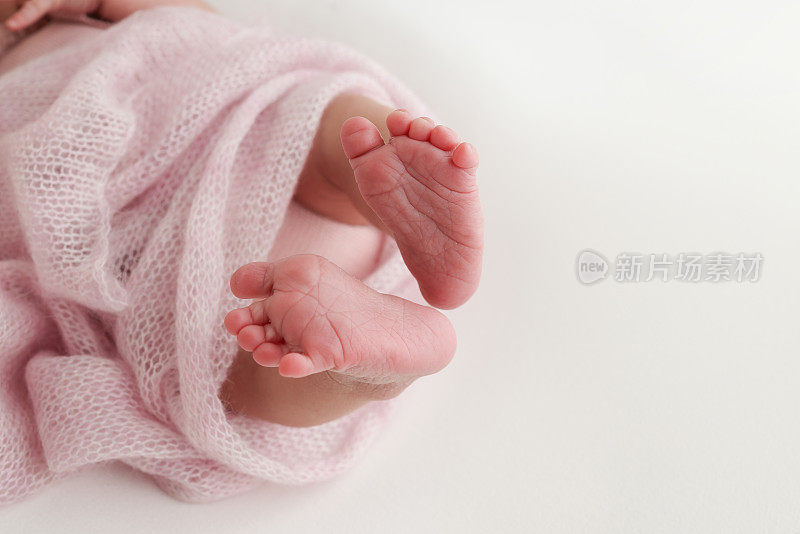 小的，可爱的，裸露的脚趾，脚跟和新生儿的脚的特写。宝宝的脚踩在粉红色柔软的被单和毯子上。新生儿腿的细节。专业的微距横向摄影工作室。