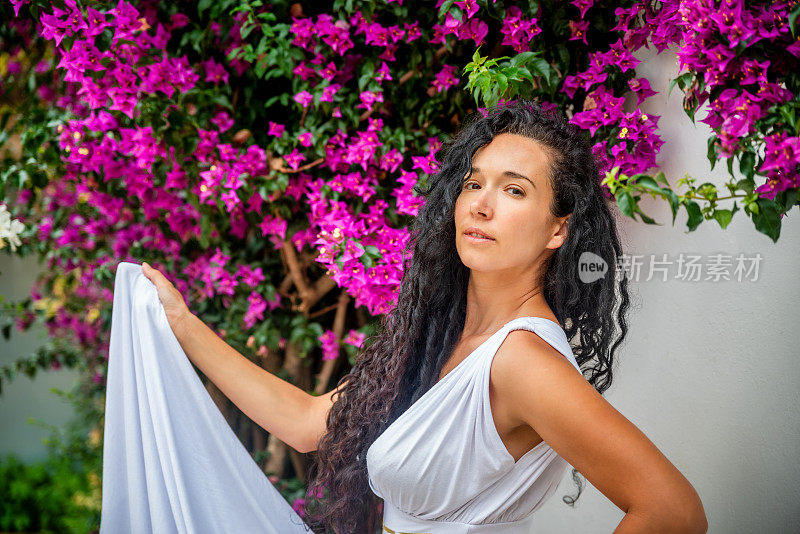 美丽的葡萄牙女子拿起裙子，在花园前开着紫罗兰花