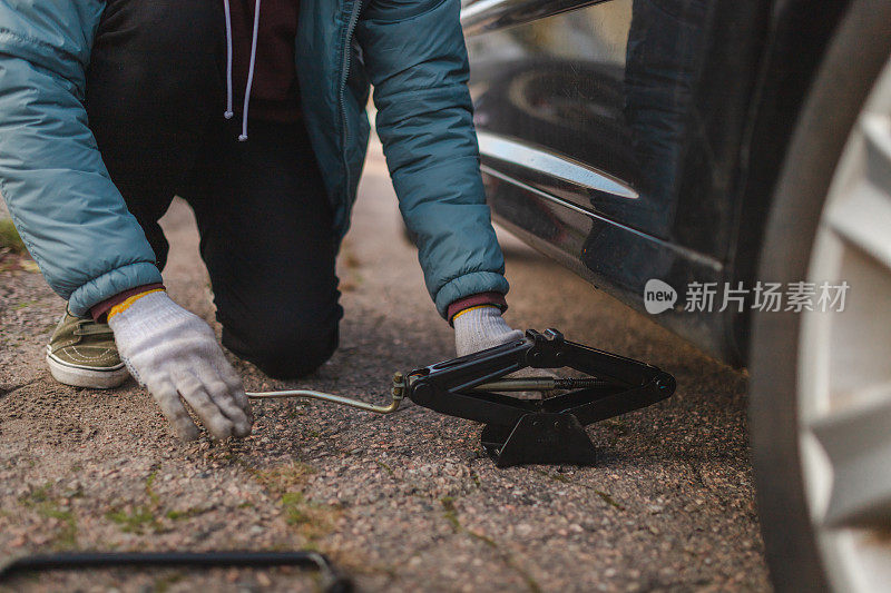 一个年轻人用汽车千斤顶在户外抬起他的车的特写