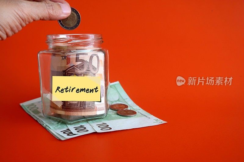 手将欧元硬币放入装有现金的玻璃瓶中，橙色背景上写着“退休”，为退休储蓄少量钱的概念，理财规划