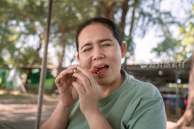 近距离拍摄的成年亚洲妇女穿着绿色t恤，坐在当地一家餐馆吃僵硬的食物，感觉疼痛引起的牙痛症状。