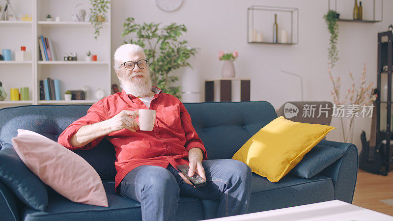 当代的爷爷在家里舒舒服服地坐在沙发上，一边看电视一边喝茶