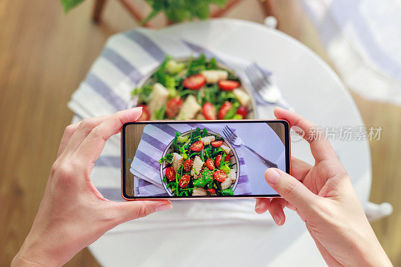一名亚洲女性用智能手机拍下美味的自制健康沙拉，然后在家里享用