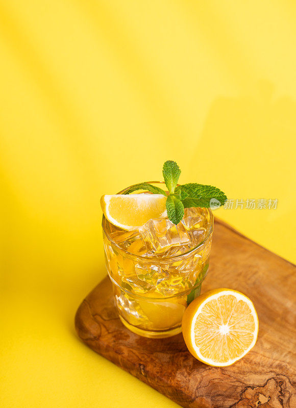 一杯加柠檬和薄荷的冰茶，放在黄底带阴影的木板上。