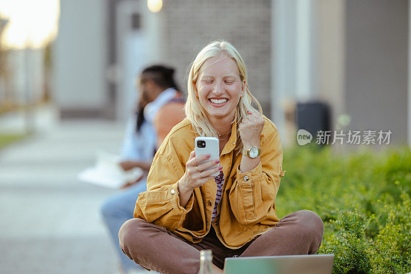 年轻的女学生在校园里的长凳上使用笔记本电脑和智能手机