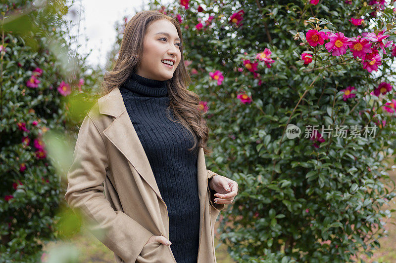 韩国女人微笑着旅游博主网红在韩国济州岛的玫瑰花园公园散步，冬天她在韩国济州岛花园享受旅游旅行
