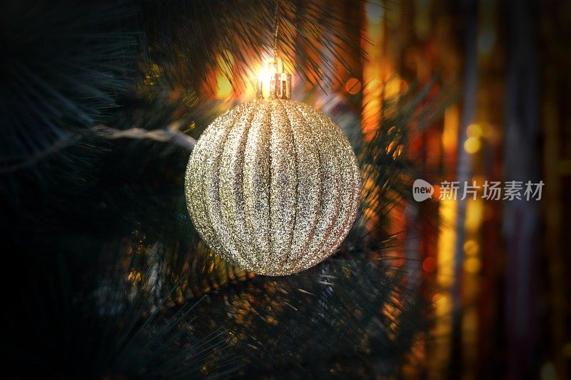 一个金色闪闪发光的三维条纹迪斯科球或圣诞装饰物的特写，悬挂在中央，在水平背景中有景深的黄色灯光
