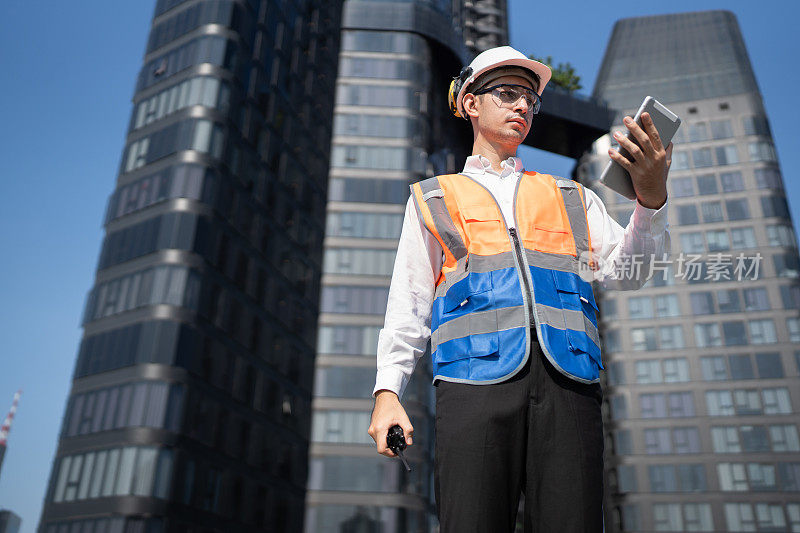 肖像亚洲的男工程师穿着防护工作服，正在屋顶大楼用平板电脑和对讲机进行系统检查