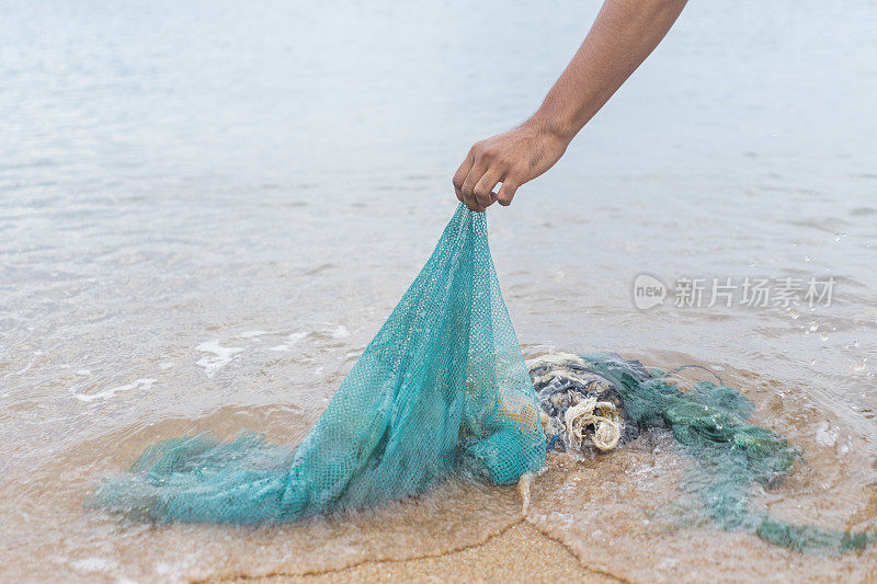 未经辨认的人士在海边收集渔网垃圾，以便妥善处理。被塑料垃圾污染的海滩肮脏区域造成了环境问题，由一名志愿者拯救。