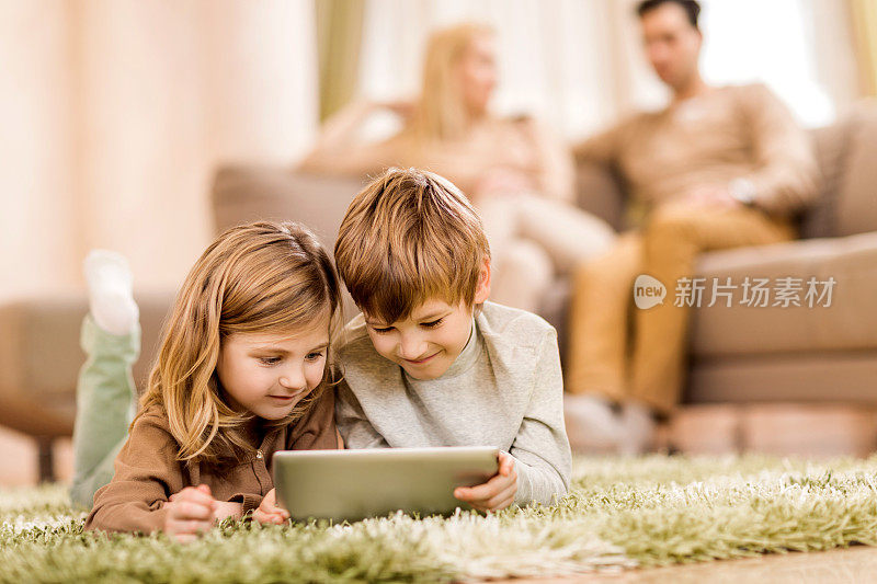 孩子们躺在地毯上使用数码平板电脑。