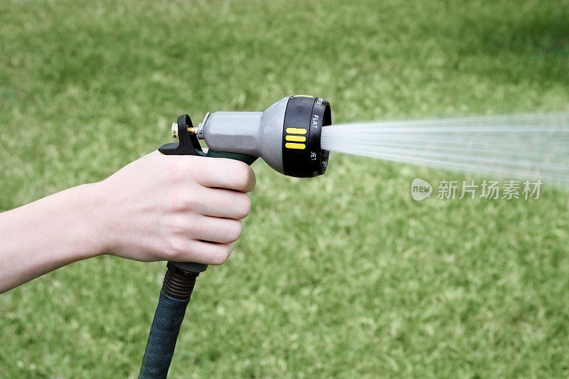 手持带喷嘴的软管喷洒水，浇灌草坪。