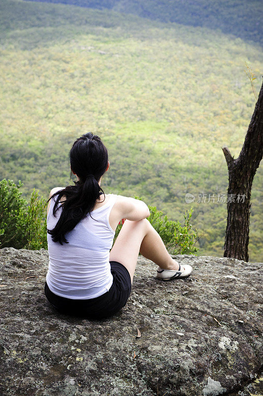 徒步女坐在看风景照片从背后