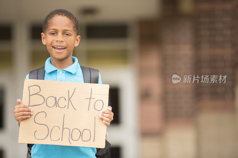 非洲后裔，一个小男孩拿着学校的牌子。