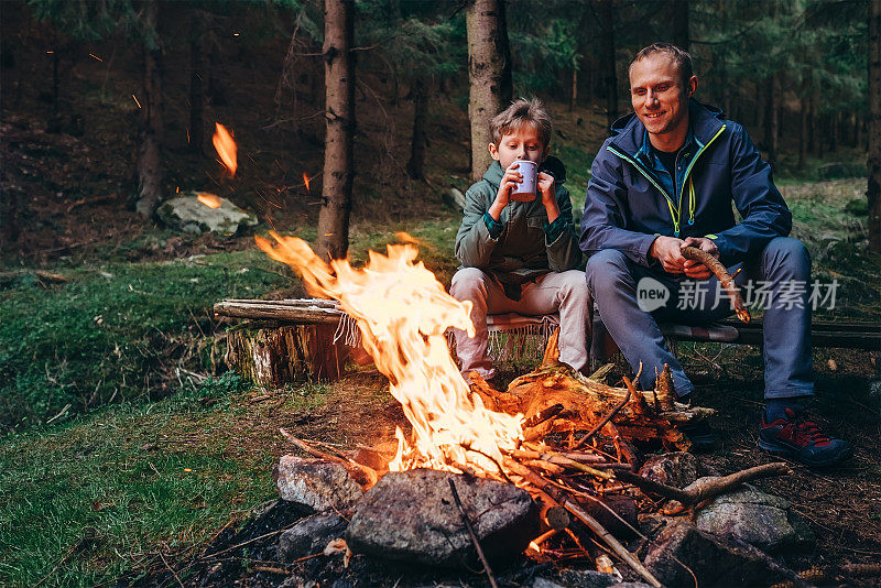 父亲和儿子在篝火旁温暖的森林野餐