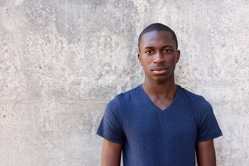 一个年轻的非洲人靠在灰色的墙上