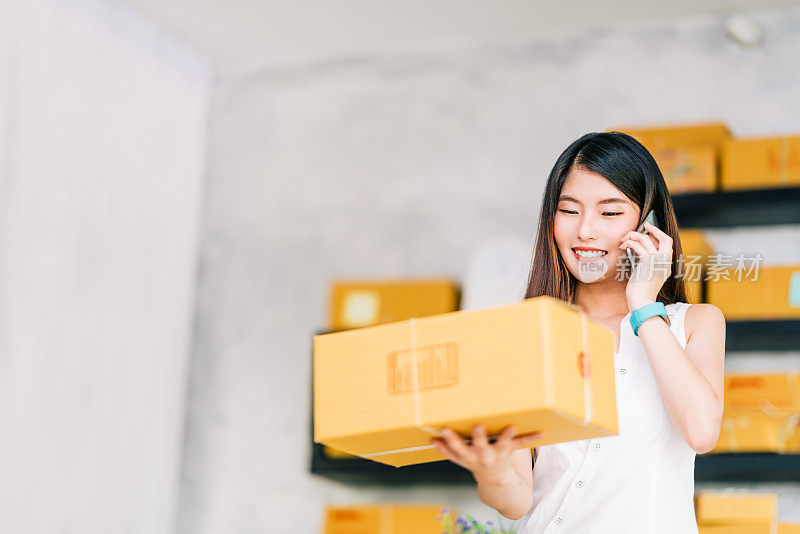 小企业主，亚洲妇女拿着包装盒，用移动电话接收采购订单，在家里办公。在线营销交付，创业中小企业企业家或自由职业者的概念