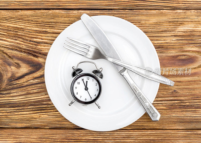 闹钟用叉子、刀和盘子放在桌上。前视图。时间吃。