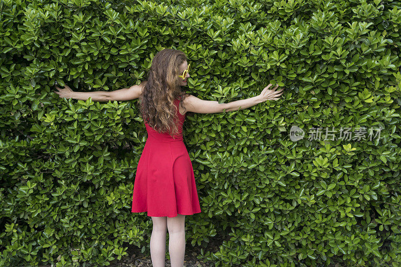 穿着红色裙子的快乐女人拥抱着一个大灌木丛