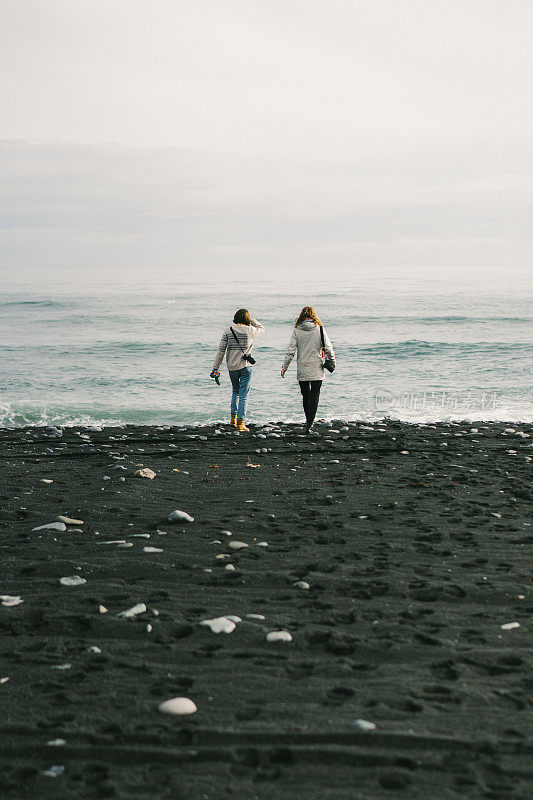 在Jokulsarlon附近的海滩上行走的妇女被冰山覆盖