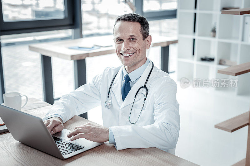 满意自信的医生坐着使用笔记本电脑。