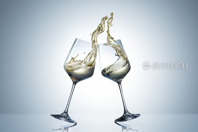 敬酒手势两个白葡萄酒杯和大溅。酒精的概念。灰色背景下的两杯酒
