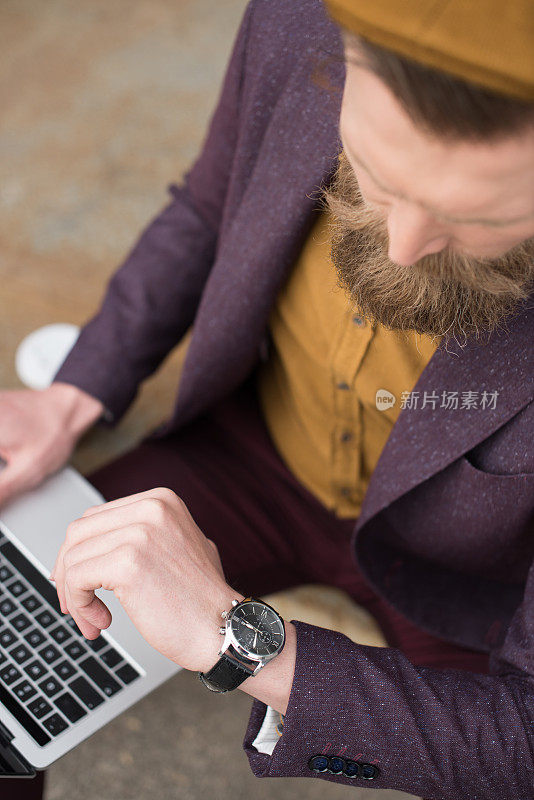 一个留着老式小胡子的商人一边摆弄着笔记本电脑一边看手表