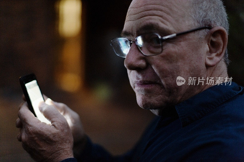 戴眼镜的老人在晚上用智能手机