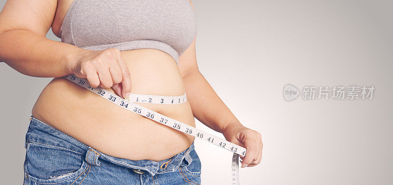 拿着卷尺的胖女人。体脂百分比用卷尺测量脂肪。
