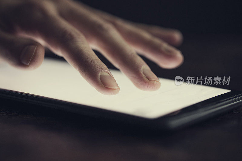 女性手握现代智能手机的特写，手指在晚上的触摸屏上。水平，模糊的背景，散景效果。