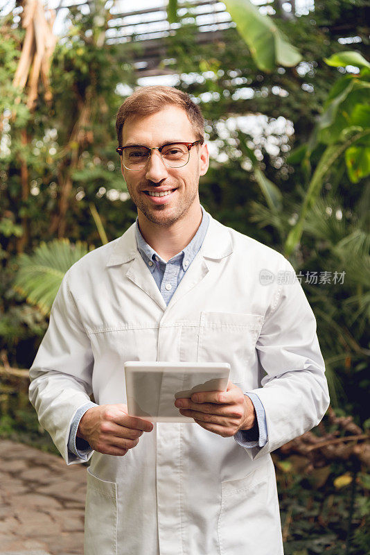 微笑英俊的科学家在白大褂和眼镜持有数字平板电脑在橘子里